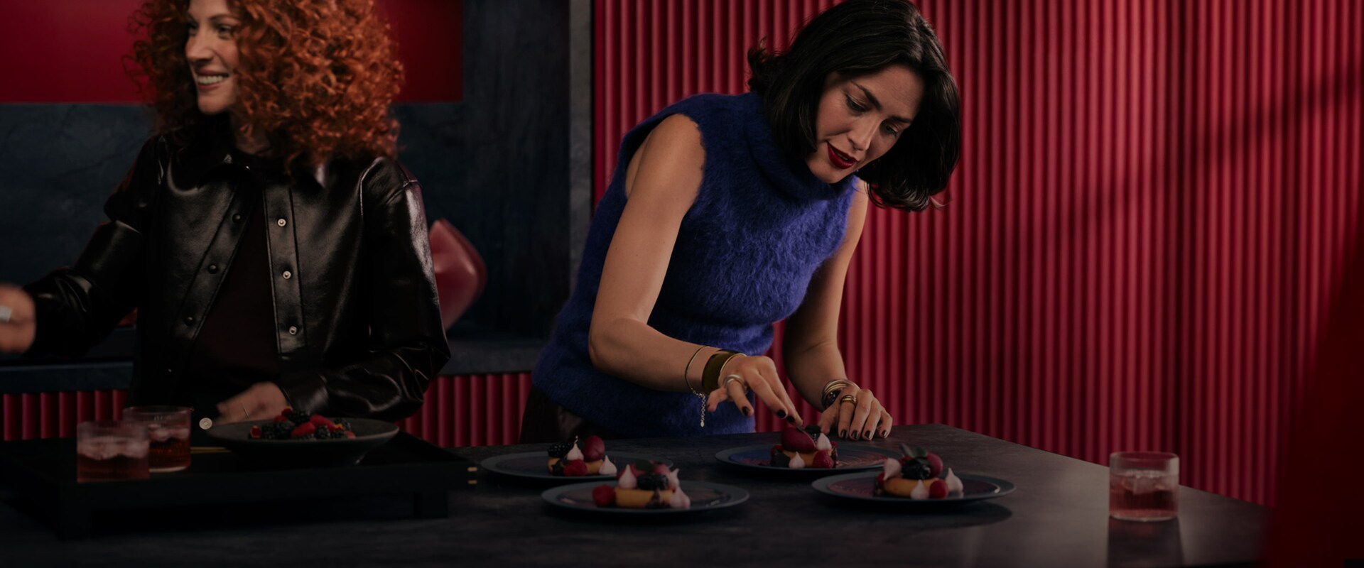 Kaksi naista valmistaa jälkiruokia tummalla keittiösaarekkeella.